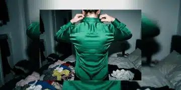 A person struggling to fit into an emerald green silk blouse, highlighting the frustration of 'effortless style' and fast fashion sizing inconsistencies.